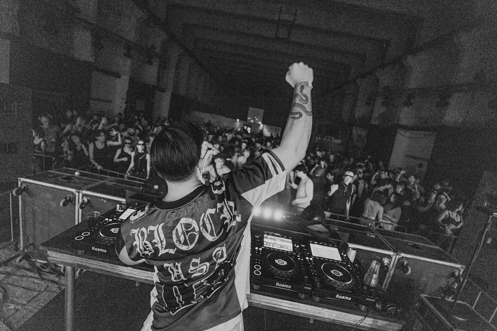 DJ met een Ultras-shirt steekt zijn vuist op boven de draaitafels, in zwart-wit