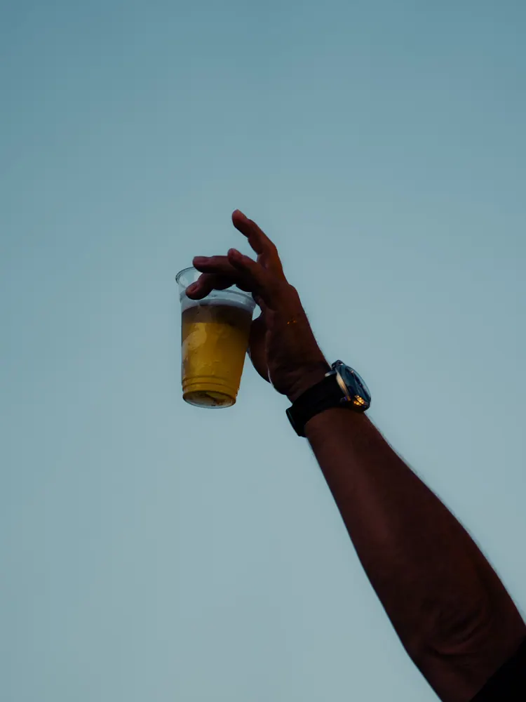 Hand met een biertje tegen een blauwe lucht