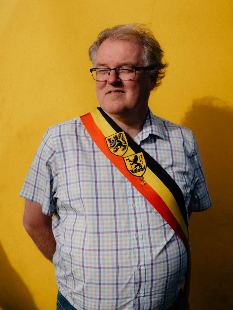 Man met een Belgische sjerp voor een gele muur