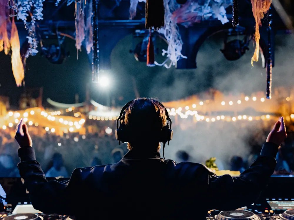 DJ met koptelefoon voor een zee van licht en publiek op LYVES Boum