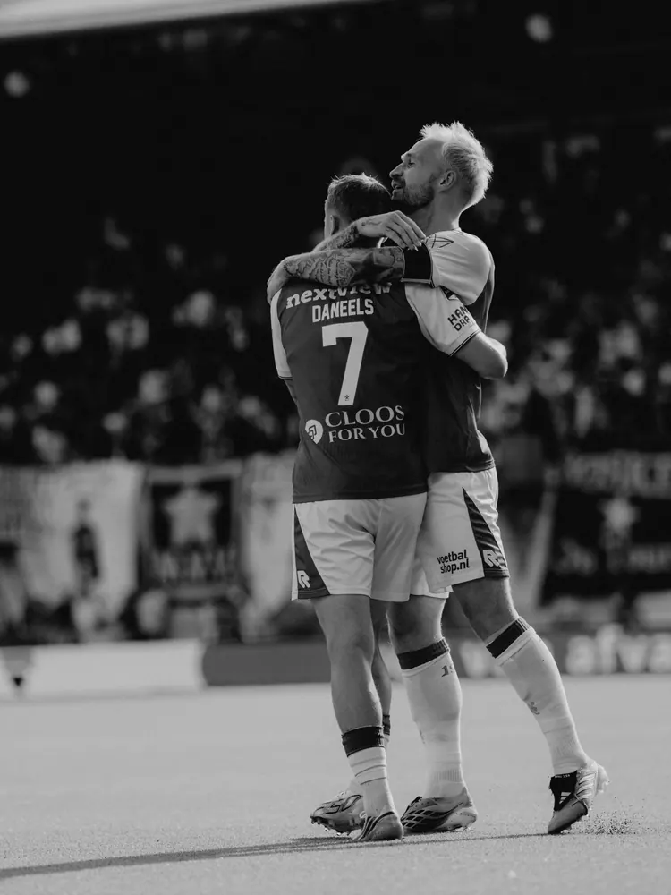 Twee spelers omhelzen elkaar na de wedstrijd, in zwart-wit
