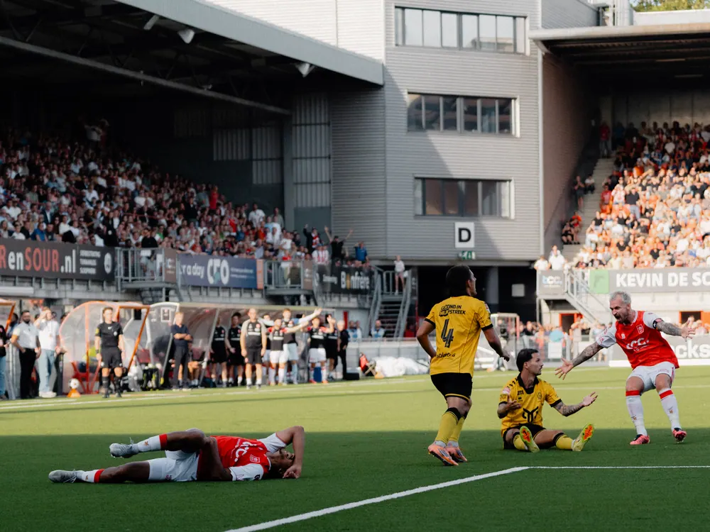 Spelers liggen op het gras na een duel voor de volle tribune