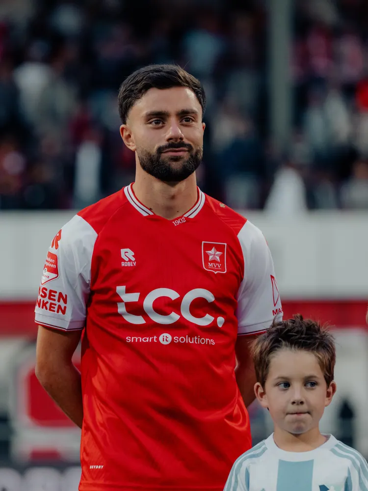 MVV-speler loopt met een jonge supporter het veld op