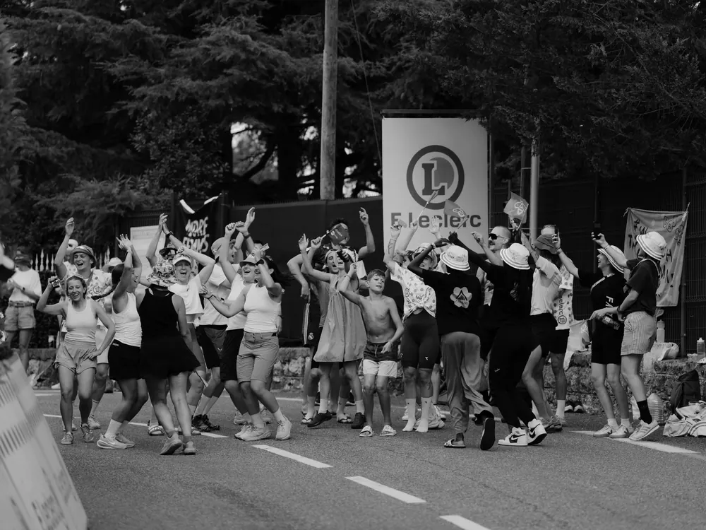 Toeschouwers dansen op de weg voor de karavaan, in zwart-wit